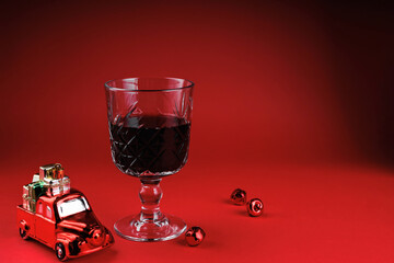 Crystal glass of red wine with toy car and Christmas bells symbolizing holiday dreams and festive joy