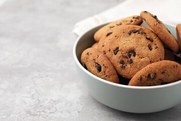 Delicious chocolate chip cookies in bowl on gray textured table, closeup. Space for text