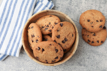 Delicious chocolate chip cookies in bowl on gray textured table, top view