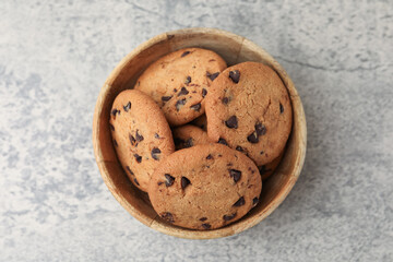 Delicious chocolate chip cookies in bowl on gray textured table, top view