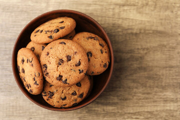 Delicious chocolate chip cookies in bowl on wooden table, top view. Space for text
