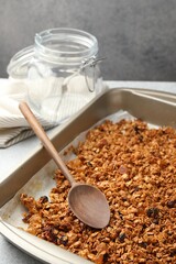 Tasty granola with dried fruits and spoon in tray on light grey table, closeup