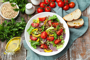 Delicious lentil salad and ingredients on wooden table, flat lay