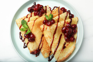 Delicious crepes with cherry jam and chocolate on white table, top view
