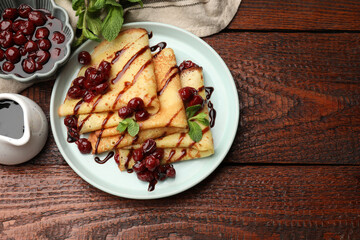 Delicious crepes served with cherry jam and chocolate on wooden table, flat lay. Space for text