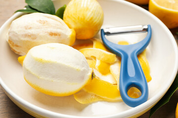 Fresh lemons with zest, peeler and leaves on wooden table, closeup