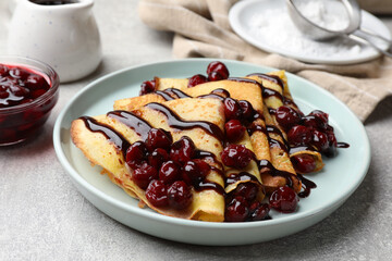 Tasty crepes with cherries and chocolate served on light table, closeup