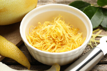 Bowl with lemon zest, fresh fruit, leaves and zester on wooden table, closeup