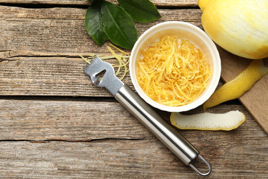 Bowl with lemon zest, fresh fruit, leaves and zester on wooden table, flat lay