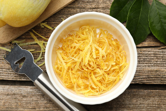 Bowl with lemon zest, fresh fruit, leaves and zester on wooden table, flat lay