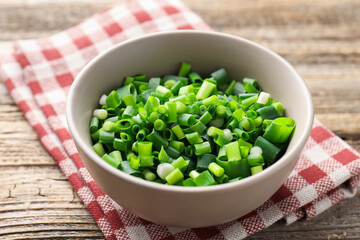 Bowl with cut green onions on wooden table, closeup
