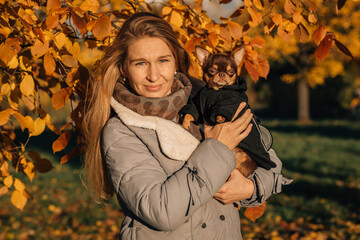 Caucasian woman holding small dog in autumn park, calm medium portrait