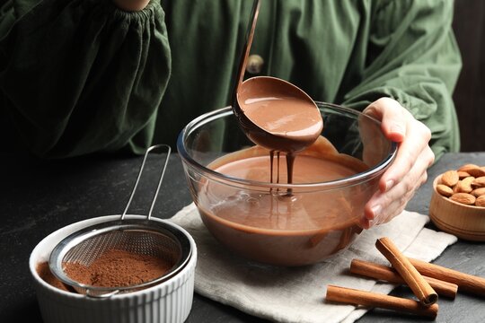 Woman taking liquid chocolate dough ladle at black table, closeup