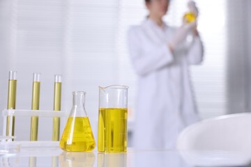 Glassware with motor oil on table and scientist working in laboratory, selective focus