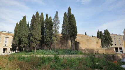 Rome, Italy - 12 January 2025. The Mausoleum of Augustus stands partially buried and ringed by cypress trees, blending ancient stone with nearby modern city structures.