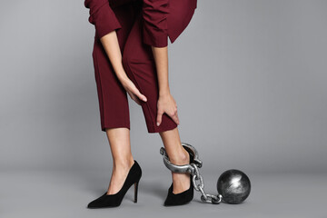 Businesswoman with metal ball and chain on her leg against grey background, closeup