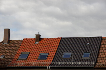 Obraz premium Rooftops of residential buildings showcasing a mix of red and dark tiles under a cloudy sky, highlighting architectural diversity and texture in urban design