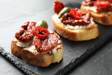 Delicious bruschettas with cream cheese, sun-dried tomatoes, chili pepper and green olives on table, closeup