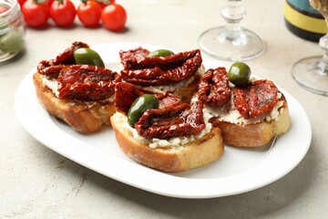 Delicious bruschettas with cream cheese, sun-dried tomatoes and green olives on gray table, closeup