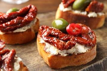 Delicious bruschettas with cream cheese, sun-dried tomatoes, chili pepper and green olives on wooden table, closeup