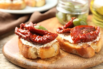 Delicious bruschettas with cream cheese, sun-dried tomatoes and green olives on table, closeup