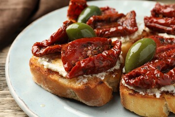 Delicious bruschettas with cream cheese, sun-dried tomatoes and green olives on table, closeup