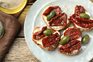 Delicious bruschettas with cream cheese, sun-dried tomatoes and green olives on wooden table, flat lay