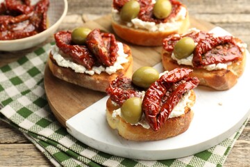 Delicious bruschettas with cream cheese, sun-dried tomatoes and green olives on table, closeup