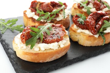 Delicious bruschettas with cream cheese, sun-dried tomatoes and arugula on white table, closeup