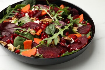 Delicious salad with beetroot, spinach, arugula, cheese, walnuts, carrot and pomegranate seeds on white table, closeup