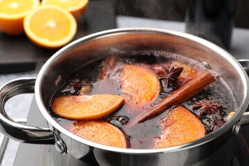 Tasty mulled wine cooking in pot on stove, closeup