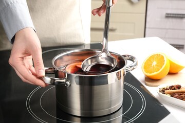 Woman cooking mulled wine in pot on stove, closeup