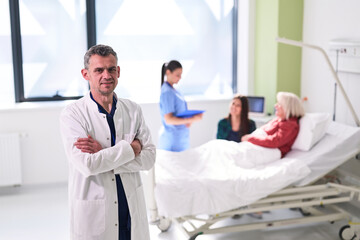 Obraz premium Surgeon stands confidently in modern hospital room while nursing staff attend to patient in bed