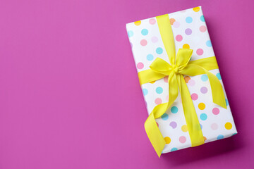 Beautiful gift with bow on violet background, top view. Space for text