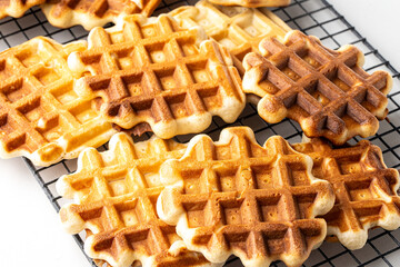Belgian waffles on a black wire rack on a white table. Preparing a delicious breakfast.