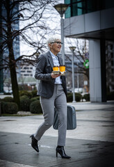 Businesswoman walking with coffee and bag in city