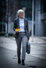 Businesswoman walking with coffee and bag in city