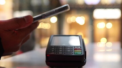 Close up of a person making a secure contactless payment with a smartphone on a pos terminal in a store, using nfc technology for a quick and easy electronic transaction at checkout - Powered by Adobe