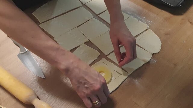A woman wraps a pineapple wedge in puff pastry. Food