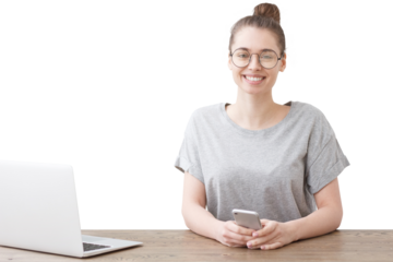 Smiling woman in glasses sitting at a wooden table holding a smartphone and looking at the camera