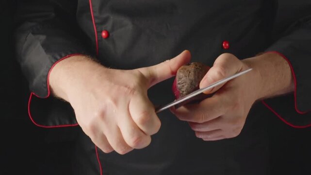 A person in a black chef jacket is holding a beetroot in one hand and slicing it with a knife in the other hand. The focus is on the preparation of the vegetable.