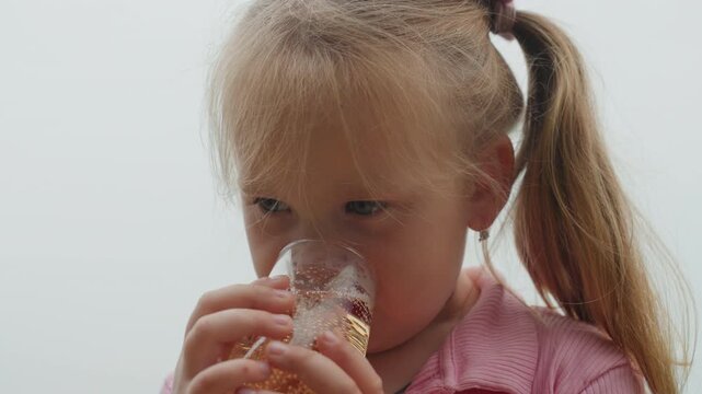 white girl tasting drink with caution tiny taster roleplay, first sip, thoughtful pause, bubbles rising in glass, amber liquid, pink shirt, pigtails, soft background, range of emotional reaction