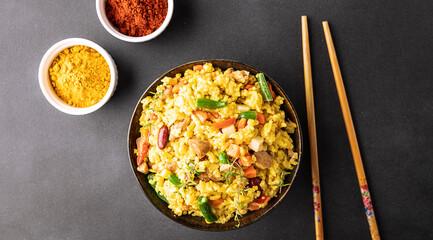 Stewed rice with meat and assortment on vegetables and spices in dark ceramic bowl on black stone table top view. Tasty homemade food concept.