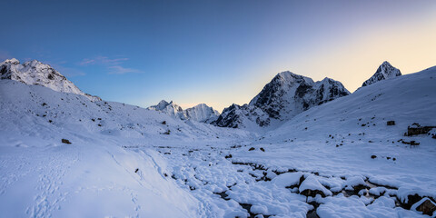 Panoramic view of the covered by snow Lobuche village surroundings in twilight after sunset. Cholatse, Tabuche peak and other mountains behind snowy valley.