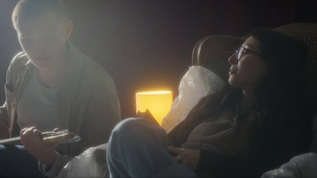 Handheld shot of young woman sitting in old armchair and talking to friend while hanging out with group of young people in abandoned house, soft focus