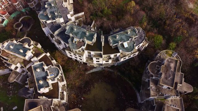 An aerial view showcases a sprawling construction site, where abandoned buildings stand empty amid overgrown greenery, whispering tales of halted progress in nature's embrace.