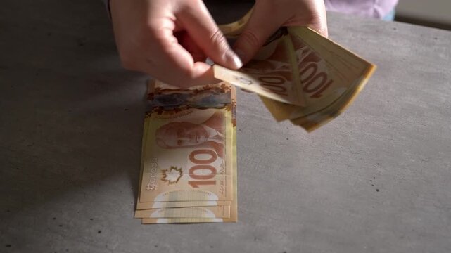 Close up slow motion shot of woman's hands counting out hundred dollar Canadian bills