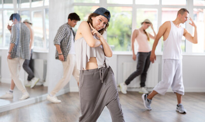 Active young girl breakdancing against other attendees of dancing classes in training hall