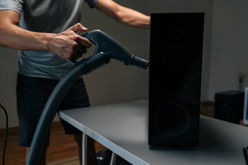 Side view of technician using vacuum cleaner to remove dust and debris from ventilation holes of...