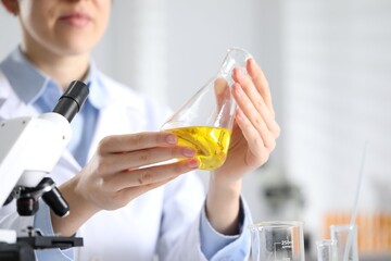 Scientist holding flask with motor oil in laboratory, closeup